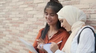 Çok ırklı kız öğrenciler sokakta ayakta dikilirken birlikte ders çalışıyorlar. Eğitim kavramı.