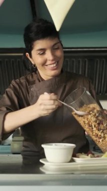 Sağlıklı gıda dükkanının mutfağında çalışırken yoğurtla mısır gevreği servis eden bir kadın. Sağlıklı yeme kavramı.