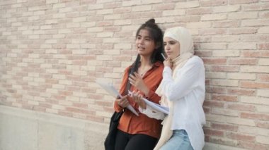 Çok ırklı bir kız öğrenci dışarıda defter yazarken fikirlerini paylaşıyor ve konuşuyor. Eğitim kavramı.