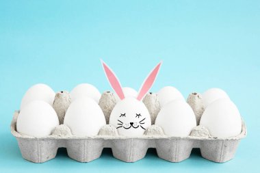 Açık mavi arka planda bir tepside yumurta beyazı ağızlıklı bir yumurta ve metin için fotokopi alanı olan tavşan kulaklı Paskalya kartı. Mutlu Paskalyalar. Tatil için hazırlık.