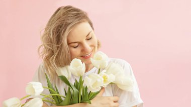 Bahar, mutluluk ve tatil kavramı. Güzel, gülümseyen bir kızın portresi. Elinde pembe bir arka planda, elinde bir buket beyaz lale tutuyordu.