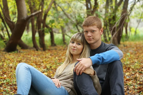 Pareja joven sentada en el follaje en el parque de otoño — Foto de Stock