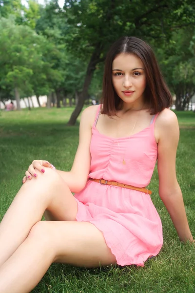 Menina bonita em vestido rosa sentar-se na grama verde — Fotografia de Stock
