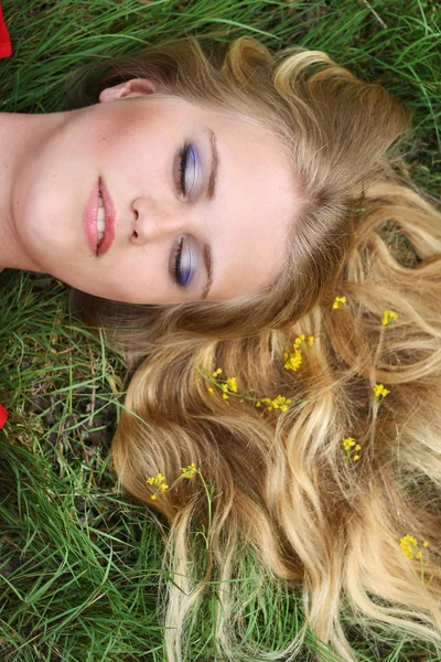 Carino bionda ragazza sdraiata in erba fiori giallo in capelli primavera — Foto Stock