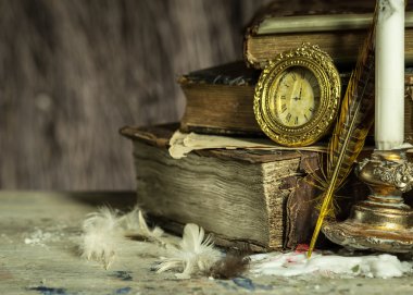 Old books, antique clock, candle in a candlestick and quill on wooden background. Vintage postcard.