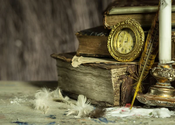 Libros antiguos, reloj antiguo, vela en un candelero y pluma sobre fondo de madera. Postal vintage . — Foto de Stock