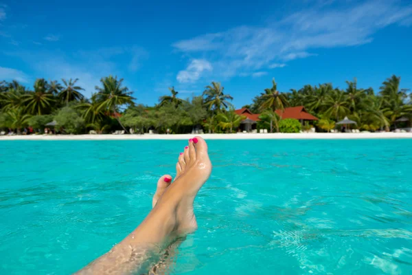 Close-up van vrouwelijke voet in het blauwe water op het tropische strand. vakantie vakantie. — Stockfoto