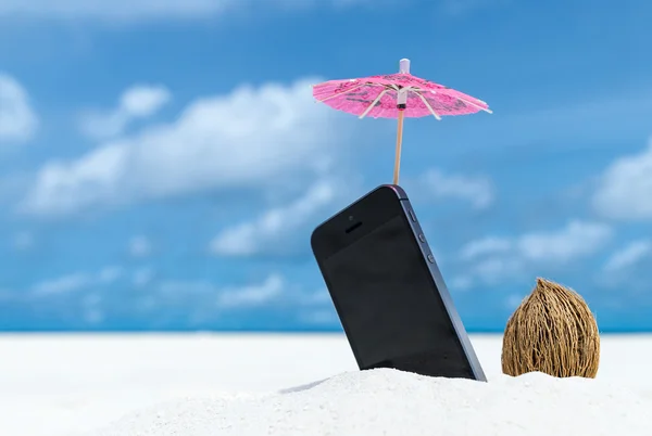 Telefono cellulare e ombrellone in spiaggia con il mare sullo sfondo — Foto Stock