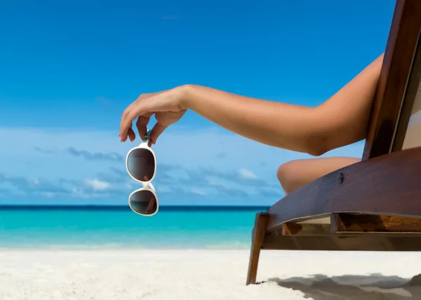 年轻的女孩躺在沙滩椅上，眼镜在热带岛屿上的手 — 图库照片