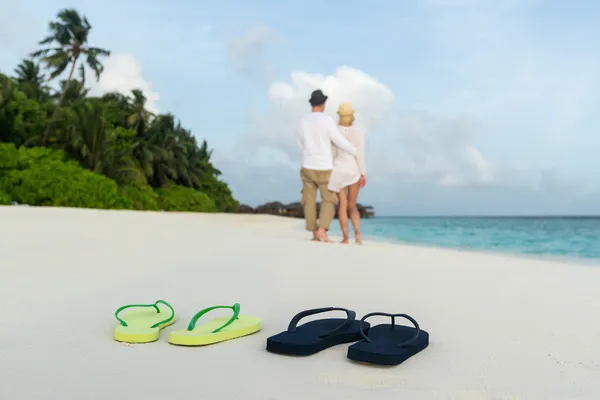 Romantic couple hug on sea sand beach against male and female flip flops closeup — Stock Photo, Image