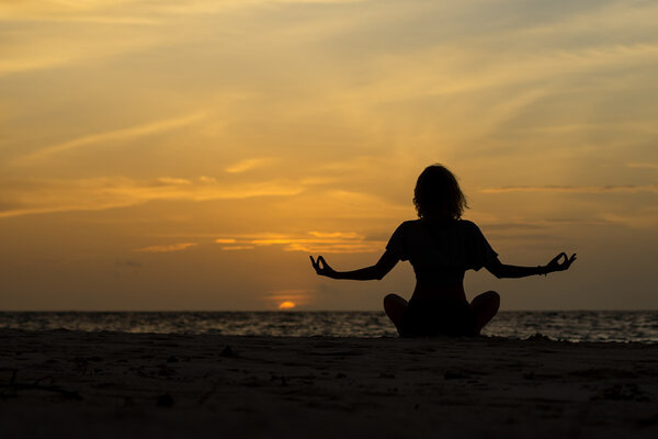 Yoga woman sitting on sea coast at sunset.