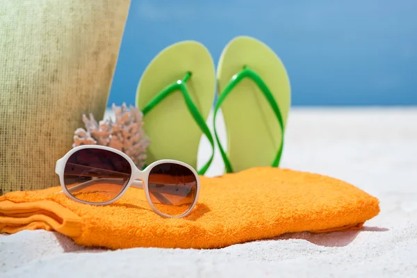 Summer beach bag with coral,towel,sunglasses and flip flops on sandy beach — Stock Photo, Image