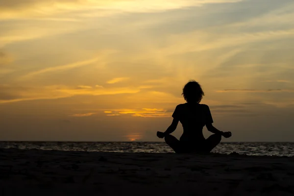 Yoga vrouw zittend op Zeekust bij zonsondergang. — Stockfoto