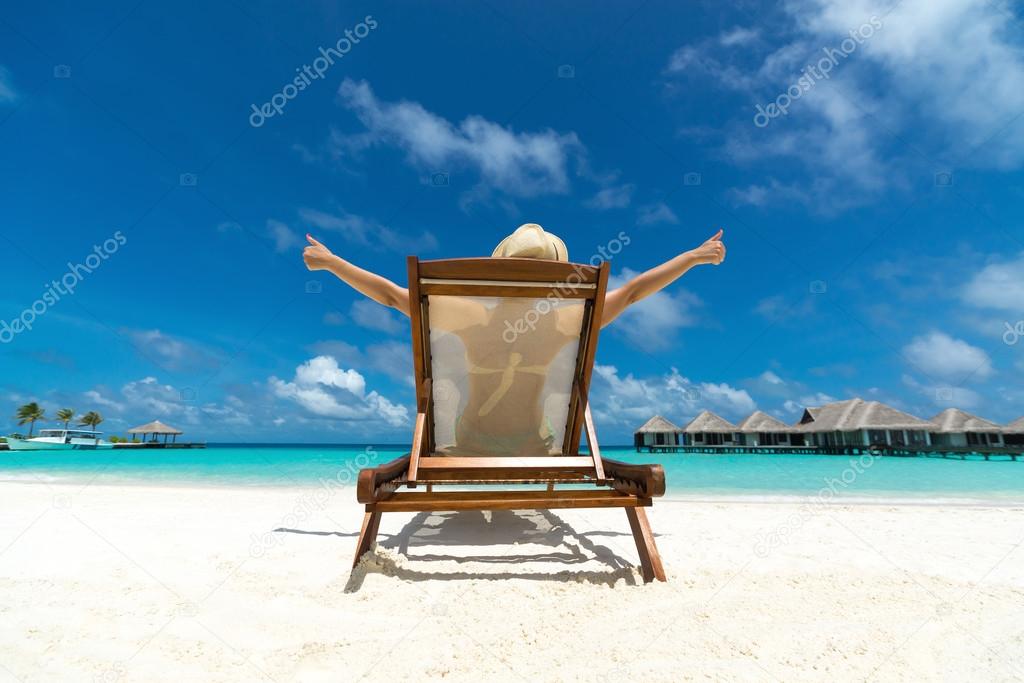 Young girl lying on a beach lounger his arms making 'thumbs up' on the tropical island