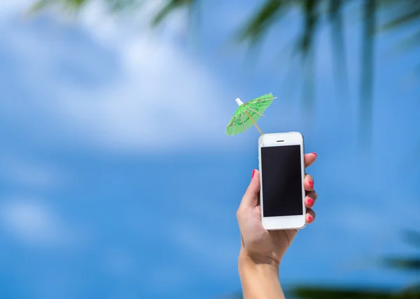 Kvinna hand visar mobiltelefon och cocktail paraply på himlen i bakgrunden — Stockfoto