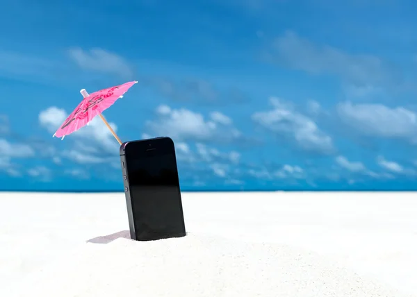 Telefono cellulare e ombrellone in spiaggia con il mare sullo sfondo — Foto Stock