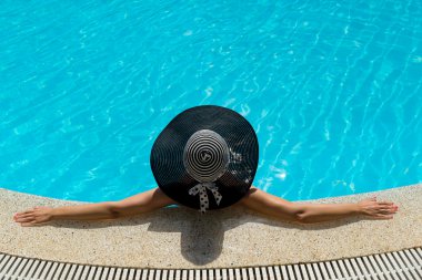 Şapkalı kadın havuzda dinleniyor.