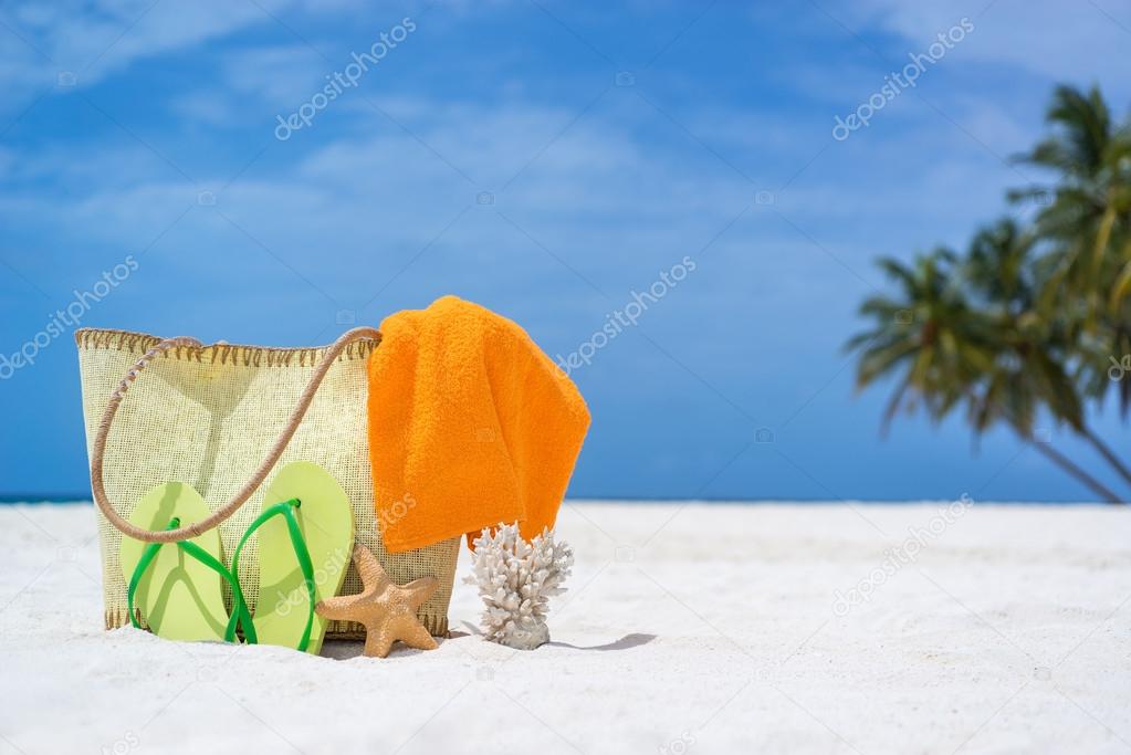 Summer beach bag with starfish,towel,sunglasses and flip flops on sandy beach