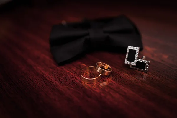 Černý motýlek, svatební zlaté prsteny na hnědém dřevěném pozadí — Stock fotografie