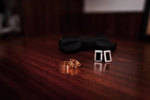 Black bow tie, wedding gold rings on brown wooden background — Fotografia de Stock