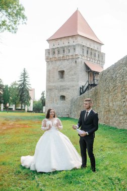 Yeni evliler parkta yürüyor, sarılıp öpüşüyorlar.