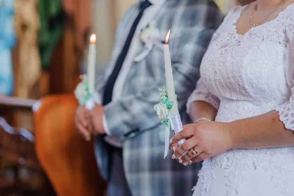 De bruid en bruidegom houden stralende kaarsen vast tijdens de ceremonie in de kerk. Handen van pasgetrouwden met kaarsen in de kerk. Kerkelijke religieuze details. Tradities — Stockfoto