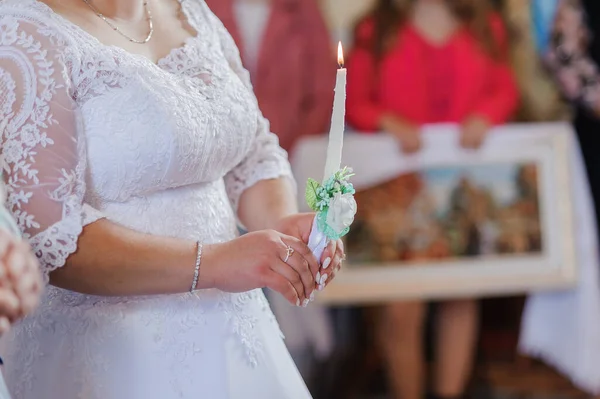 Pengantin perempuan dan laki-laki memegang lilin bersinar selama upacara di gereja. Tangan pengantin baru dengan lilin di dalam gereja. Rincian keagamaan gereja. Tradisi — Stok Foto