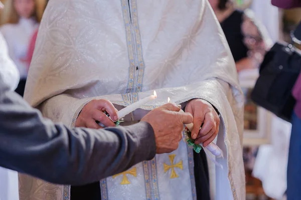 Pengantin perempuan dan laki-laki memegang lilin bersinar selama upacara di gereja. Tangan pengantin baru dengan lilin di dalam gereja. Rincian keagamaan gereja. Tradisi — Stok Foto