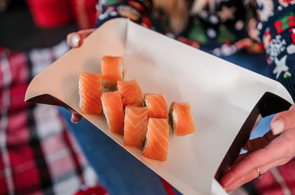 크리스마스 트리의 배경에 있는 한 소녀의 손에 쥐고 있는 초밥 — 스톡 사진