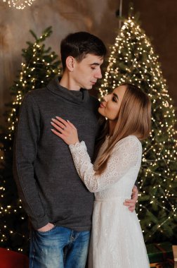 Bir erkek ve bir kız, bir Noel ağacı ve kırmızı bir kanepenin arka planında sarılıp öpüşürler.