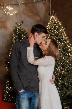 Bir erkek ve bir kız, bir Noel ağacı ve kırmızı bir kanepenin arka planında sarılıp öpüşürler.