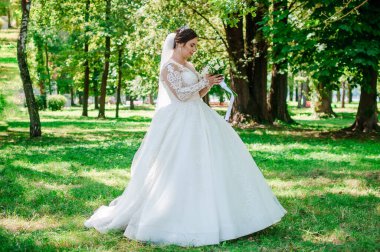 Yeşil arka planda güzel beyaz elbiseli bir gelinin portresi. Bir buket çiçekli gelin.