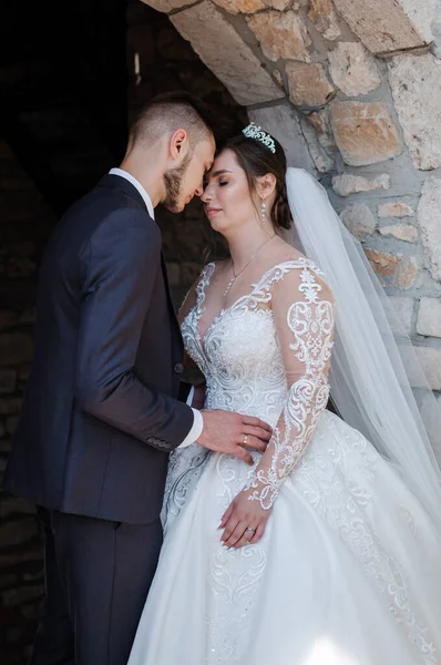 La novia y el novio abrazan y besan contra el telón de fondo de un arco de piedra. Boda —  Fotos de Stock