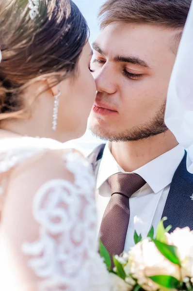 Os recém-casados abraçam e beijam sob o véu. Noiva segurando um buquê de flores — Fotografia de Stock