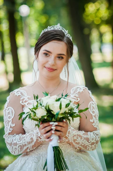 Ritratto di sposa in un bellissimo vestito bianco su sfondo verde. Sposa con un mazzo di fiori — Foto Stock