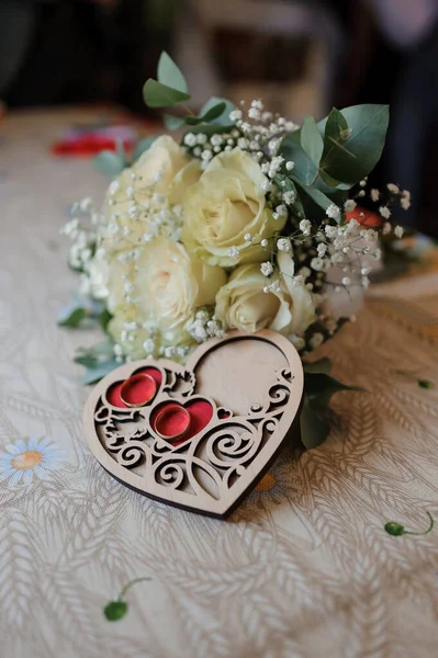 Букет белых роз невесты, пара золотых колец на деревянном подставке в форме сердца — стоковое фото