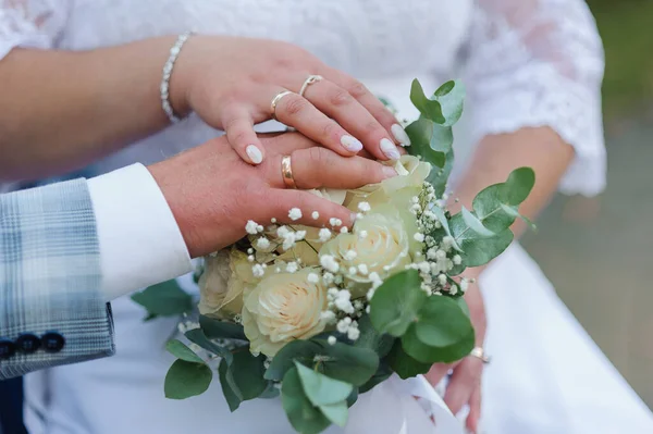 Золоті обручки, руки нареченого і нареченого на букет квітів — стокове фото