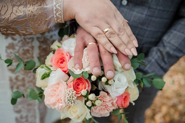 Gouden trouwringen, handen van de bruid en bruidegom op een boeket bloemen — Stockfoto