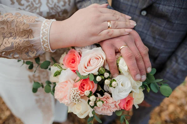 Gouden trouwringen, handen van de bruid en bruidegom op een boeket bloemen — Stockfoto