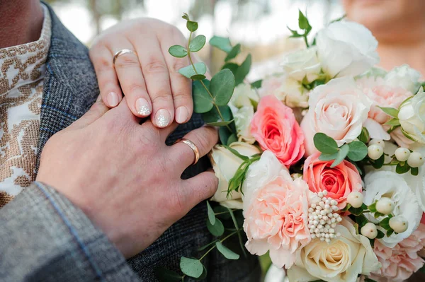 Gouden trouwringen, handen van de bruid en bruidegom op een boeket bloemen — Stockfoto