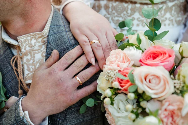 Золотые обручальные кольца, руки жениха и невесты на букете цветов — стоковое фото