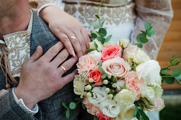 Anéis de casamento dourados, mãos da noiva e noivo em um buquê de flores — Fotografia de Stock