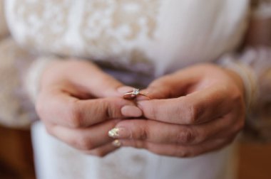 Gelinin elinde bir çift altın alyans. Alyanslar kadın elinde.