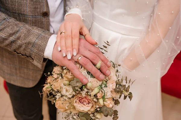 Ruce novomanželů se zlatými prsteny na kytici květin. Ruce nevěsty a ženicha na krásné kytici — Stock fotografie
