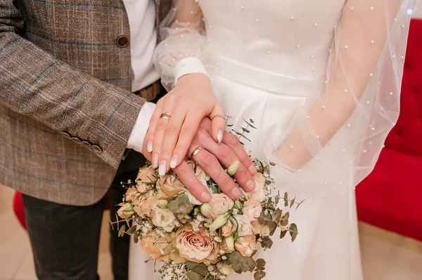 Руки молодоженов с золотыми кольцами на букете цветов. Руки жениха и невесты на красивом букете — стоковое фото