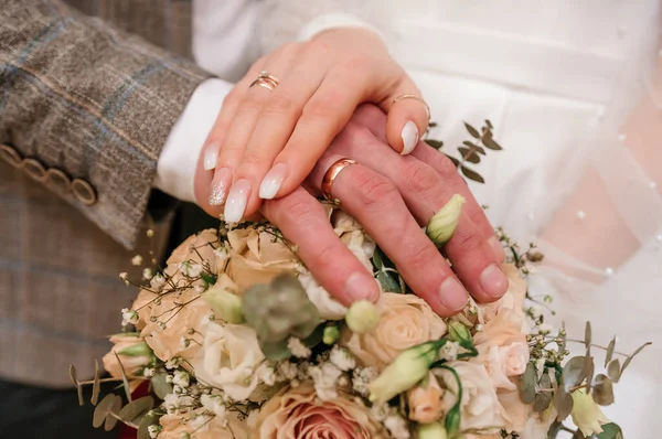 Χέρια νεόνυμφων με χρυσά δαχτυλίδια σε μπουκέτο λουλουδιών. Χέρια της νύφης και του γαμπρού σε ένα όμορφο μπουκέτο — Φωτογραφία Αρχείου