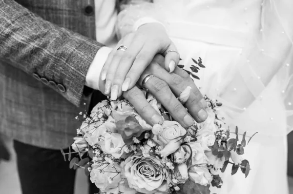 Manos de recién casados con anillos de oro en un ramo de flores. Las manos de la novia y el novio en un hermoso ramo — Foto de Stock
