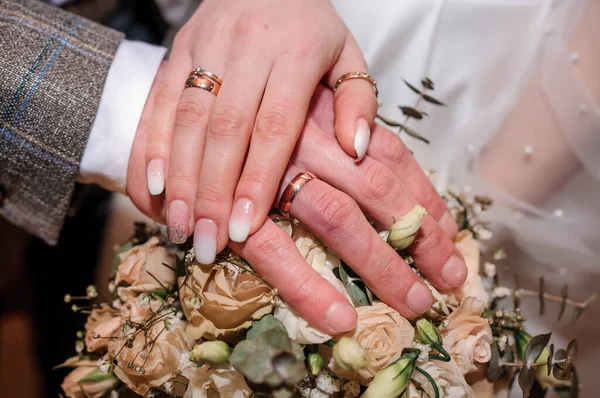 花束の上に金色のリングを持つ新婚夫婦の手。美しい花束で花嫁と新郎の手 — ストック写真