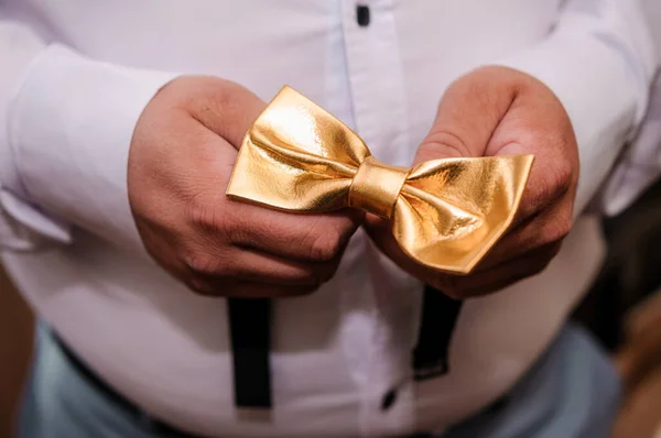 Golden bow tie in the hands of the groom. Bow tie in the hands of a man