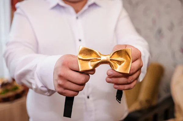 Golden bow tie in the hands of the groom. Bow tie in the hands of a man